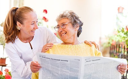 Elderly lady reading newspaper with caregiver